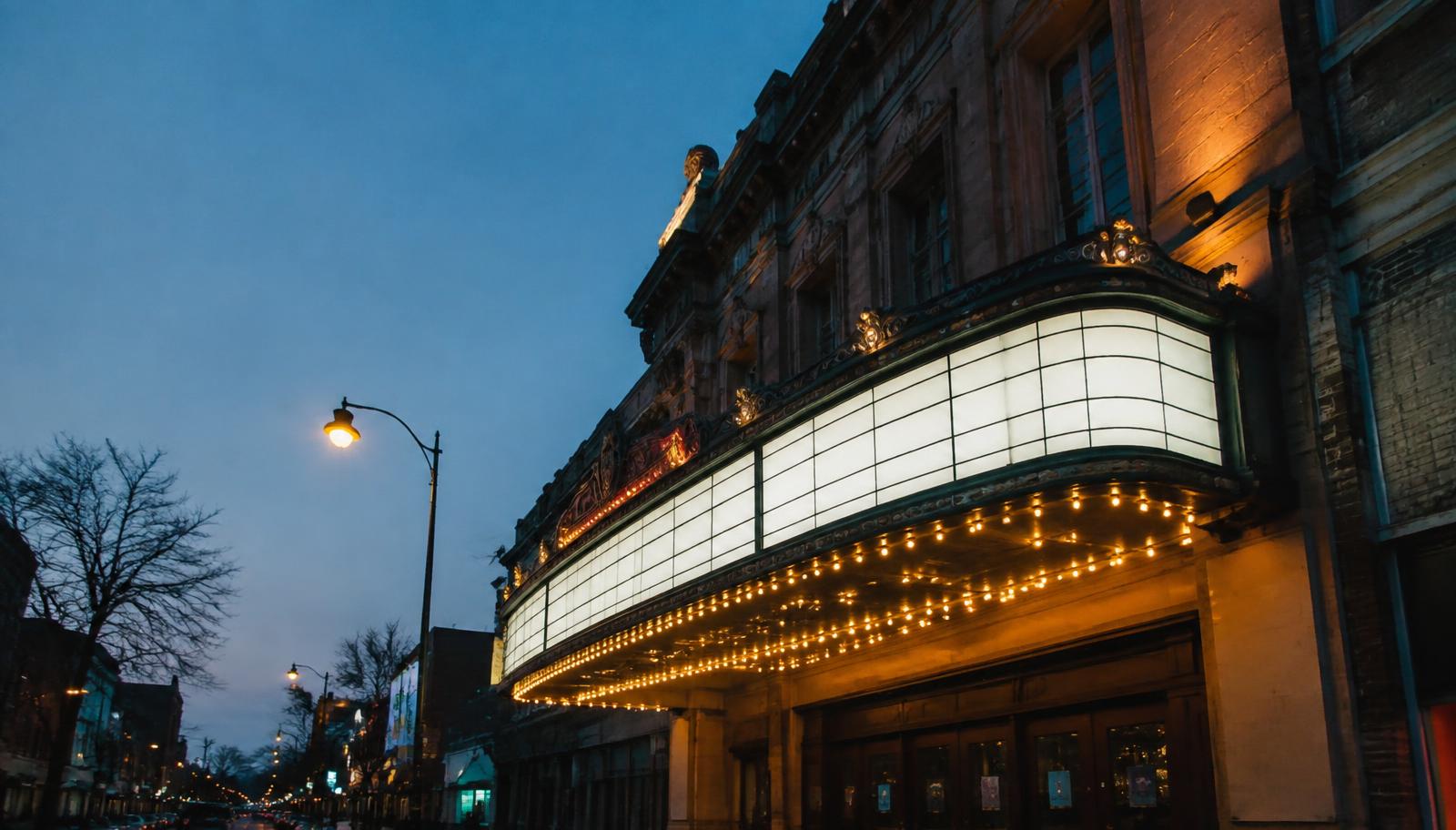 A historic theatre marquee lit at dusk above a city street.